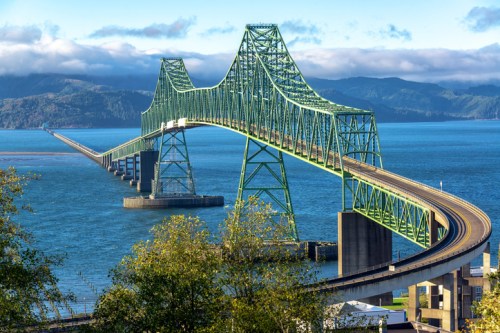 A green bridge spans over a blue body of water, connecting land with a scenic backdrop of mountains and clouds.
