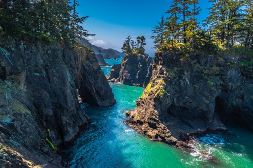 A scenic view of rocky cliffs and turquoise waters, surrounded by lush trees under a clear blue sky.