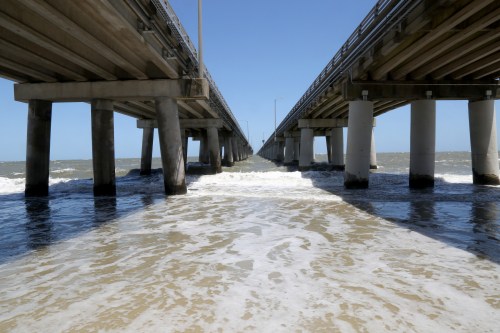 View of a pier extending over the ocean, with waves lapping at the supports and a clear blue sky above.