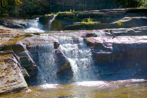 A serene waterfall cascading over rocky ledges, surrounded by lush greenery and autumn foliage.