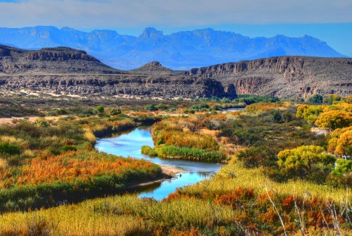 A scenic landscape featuring a winding river surrounded by colorful foliage and mountains in the background.