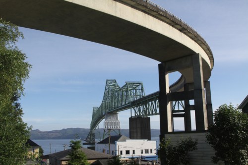 A large, curved bridge spans over a body of water, with buildings and greenery in the foreground.