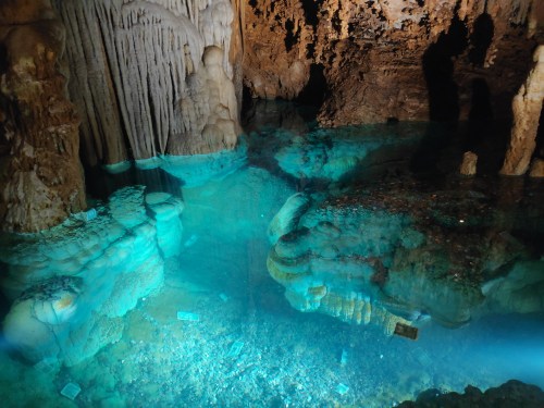 A serene underground cave with stalactites and stalagmites reflected in clear blue water.