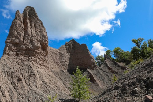 Rocky formations rise against a blue sky with scattered clouds, surrounded by greenery.
