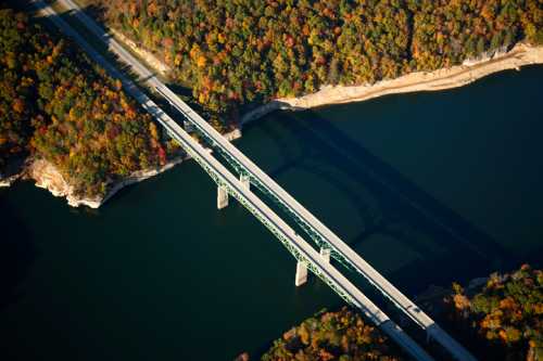 Aerial view of a green bridge spanning a river, surrounded by vibrant autumn foliage and calm waters.