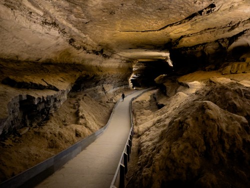 A winding pathway through a dimly lit cave, with rocky walls and a sandy floor.