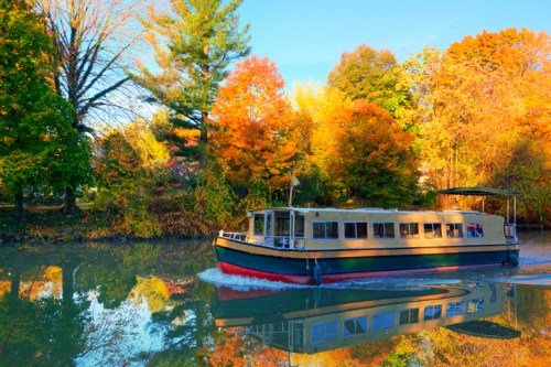 A boat glides through a calm waterway surrounded by vibrant autumn foliage.