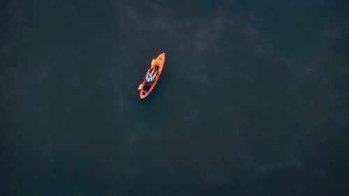 An orange kayak floats on calm, dark water, with a person seated inside.