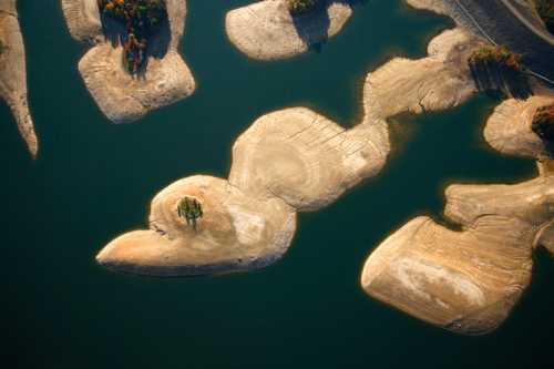 Aerial view of a serene lake with sandy islands and scattered trees, surrounded by calm blue water.