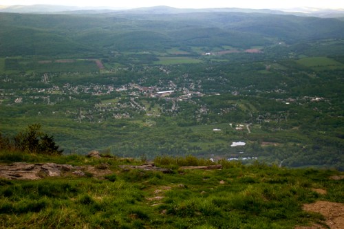 A panoramic view of a lush green valley with a small town nestled among rolling hills under a cloudy sky.