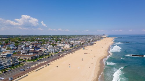 Aerial view of a beachside town with sandy shores, ocean waves, and a clear blue sky.