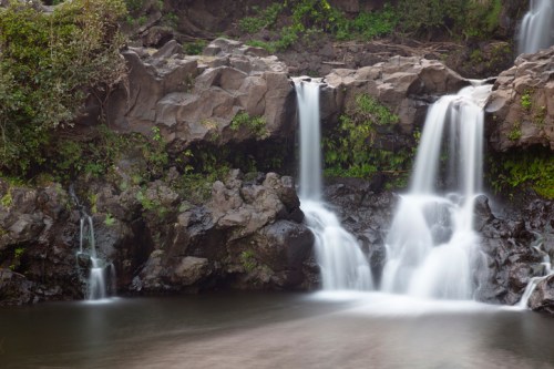 A serene waterfall cascading over rocky terrain into a calm pool, surrounded by lush greenery.
