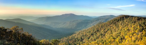 Panoramic view of rolling mountains and valleys, bathed in soft morning light with lush greenery.