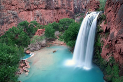 A stunning waterfall cascades into a turquoise pool, surrounded by lush greenery and red rock formations.