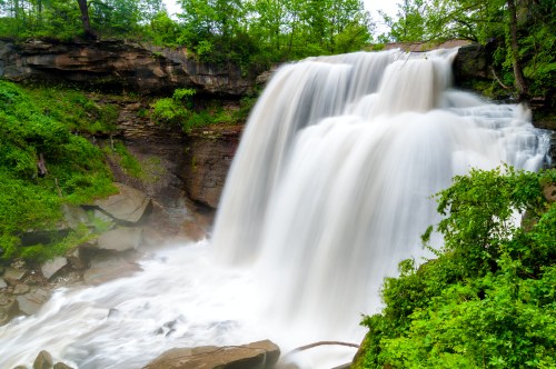 A cascading waterfall surrounded by lush greenery and rocky terrain, creating a serene natural scene.
