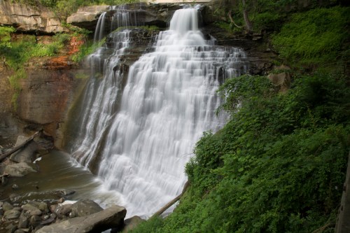 A cascading waterfall surrounded by lush greenery and rocky terrain, creating a serene natural scene.