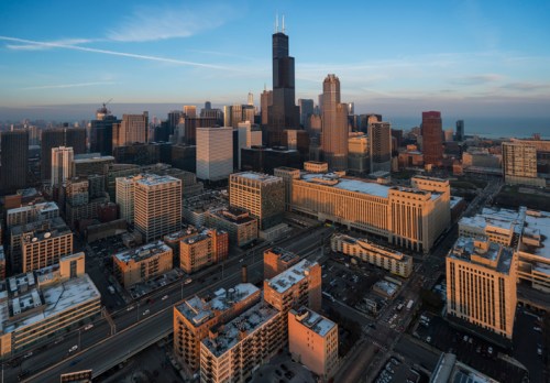 Aerial view of a city skyline at sunset, featuring tall buildings and a clear sky.