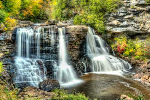 A serene waterfall cascading over rocky cliffs, surrounded by vibrant autumn foliage and a calm pool below.