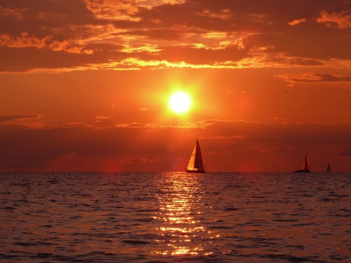 A vibrant sunset over the ocean, with sailboats silhouetted against the glowing sky.