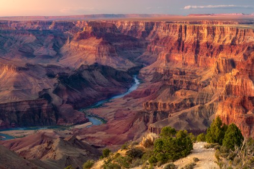 A stunning view of the Grand Canyon at sunset, showcasing layered red rock formations and a winding river below.