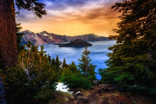 A scenic view of Crater Lake surrounded by trees, with vibrant sunset colors illuminating the sky.