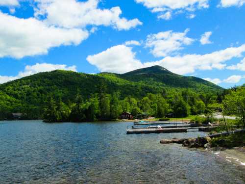 A serene lake surrounded by lush green mountains under a bright blue sky with fluffy clouds.