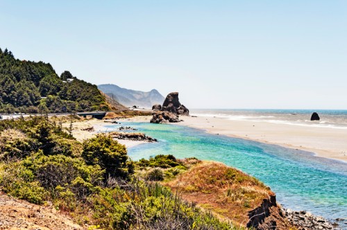 Scenic coastal view with a sandy beach, turquoise water, and rocky formations under a clear blue sky.