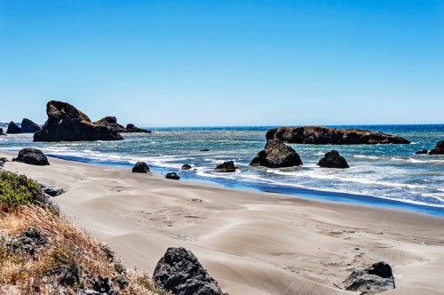 A scenic beach with sandy shores, rocky formations, and calm waves under a clear blue sky.