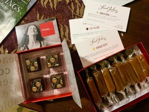 A box of chocolates with decorative pieces, alongside caramel candies and business cards on a table.