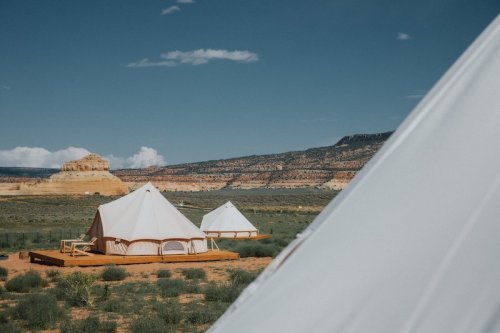 Two large white tents on wooden platforms in a desert landscape with distant rock formations and blue sky.