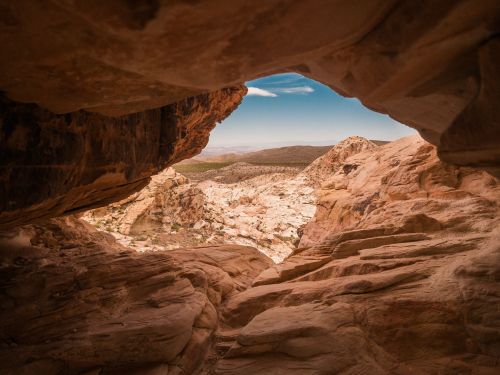 View through a rocky cave opening, revealing a vast desert landscape with distant mountains and blue sky.