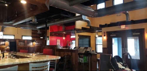 Interior of a restaurant featuring a bar, wooden accents, and exposed ductwork, with red and yellow walls.