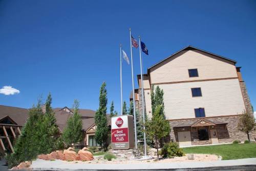 Exterior view of a Best Western Plus hotel with flags and trees under a clear blue sky.