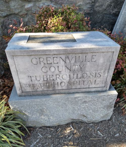 Stone monument inscribed with "Greenville County Tuberculosis Hospital Erected 1930" surrounded by greenery.