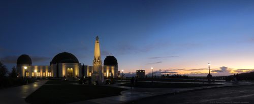 A panoramic view of a building with domes and an obelisk at dusk, illuminated against a twilight sky.
