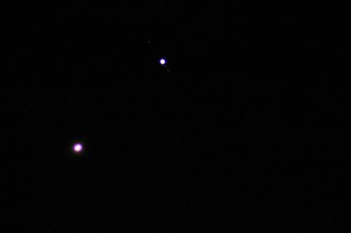 Two bright celestial bodies against a dark night sky, with one larger and one smaller, possibly planets or stars.