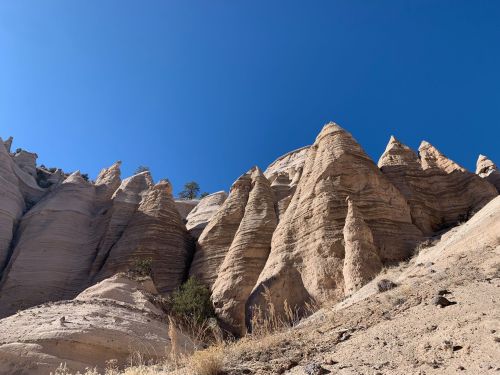 Rocky formations rise against a clear blue sky, showcasing unique, layered textures and shapes in a desert landscape.