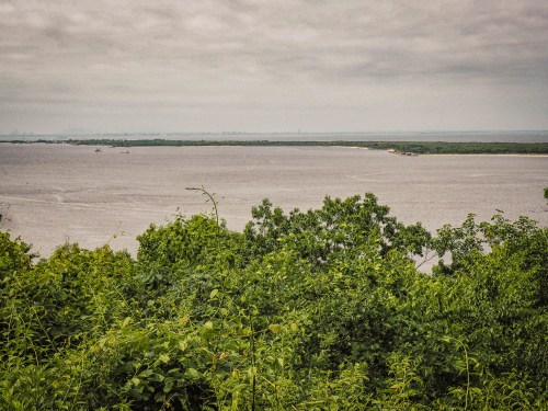 A serene view of a river surrounded by lush greenery under a cloudy sky.
