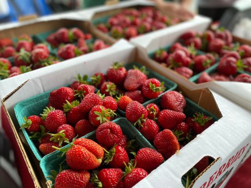 Fresh strawberries in green containers stacked in cardboard boxes at a market.