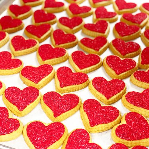 A tray of heart-shaped cookies with red sparkling icing, arranged neatly in rows.