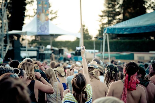 A crowd at a music festival, with a person holding up a camera to capture the performance on stage.