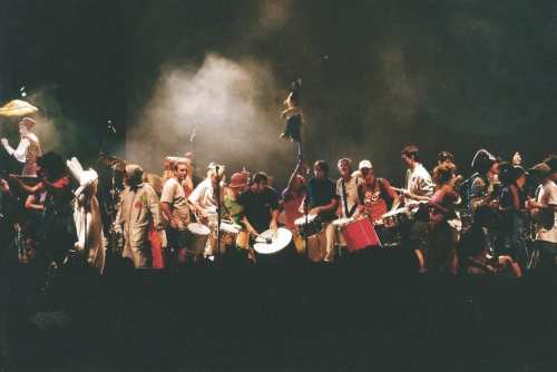 A lively group of musicians performing on stage with various instruments, surrounded by smoke and vibrant energy.