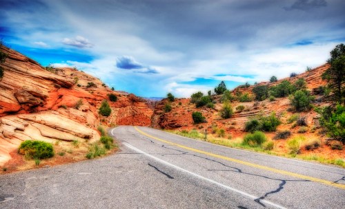 A winding road through vibrant red rock formations and green vegetation under a cloudy sky.