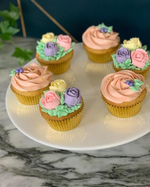 A plate of beautifully decorated cupcakes with pastel-colored frosting and floral designs on top.