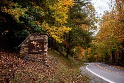 Sign for Holly River State Park at the main entrance, surrounded by colorful autumn foliage and a winding road.