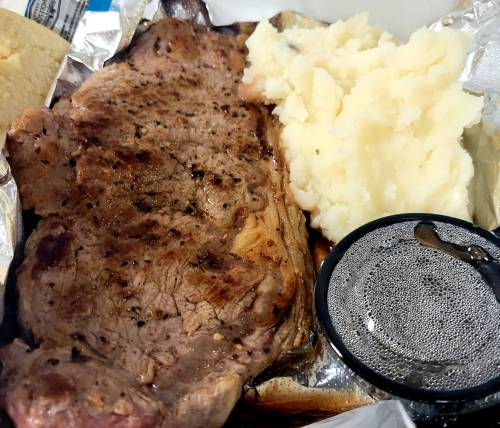 A plate featuring a grilled steak, creamy mashed potatoes, and a small container of sauce.