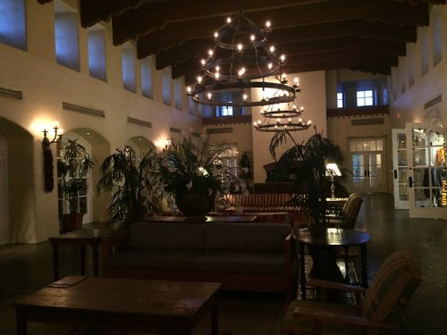 Cozy lobby with high ceilings, chandeliers, plants, and comfortable seating, illuminated by soft, warm lighting.
