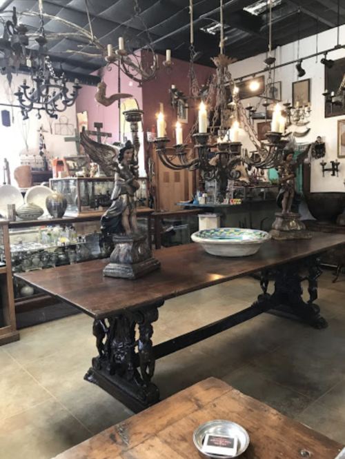 A vintage shop interior featuring a large wooden table, ornate candelabras, and various decorative items.