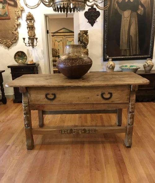 A rustic wooden table with a drawer, topped with a decorative vase, set in a vintage-style room.