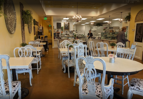 A cozy café interior with elegant white chairs, tables, and a display counter in the background.